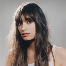 > "Portrait d’un artiste variété française en débardeur blanc sur fond gris clair, cheveux longs et décoiffés – visuel épuré Vibes Concert"