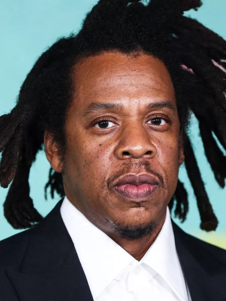 > "Portrait d’un artiste hip hop en costume noir et chemise blanche sur fond bleu clair – style épuré Vibes Concert"