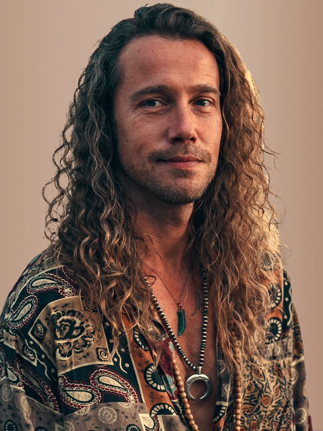 > "Portrait d’un artiste variété française en chemise à motifs cachemire, colliers bohème et cheveux longs bouclés – style éclectique Vibes Concert"