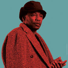 > "Portrait d’un artiste hip hop en manteau rouge à motifs chevrons, devant un fond vert émeraude – esthétique stylisée Vibes Concert"