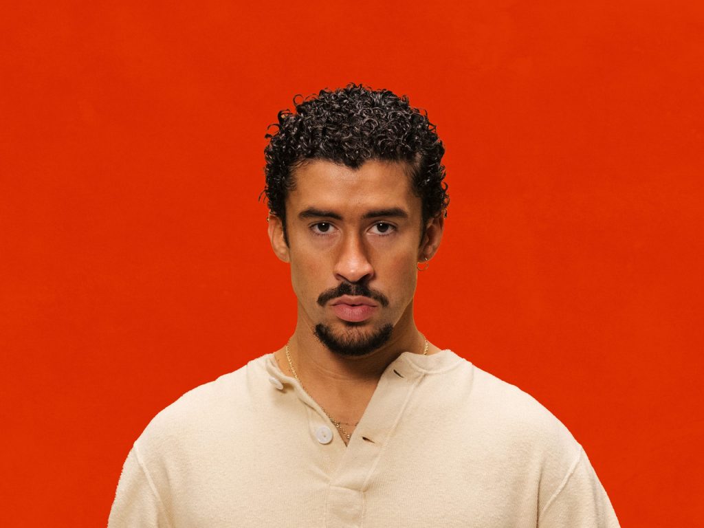 > "Portrait d’un artiste variété internationale en chemise boutonnée ivoire et collier discret, devant un fond rouge vif – visuel contrasté Vibes Concert"