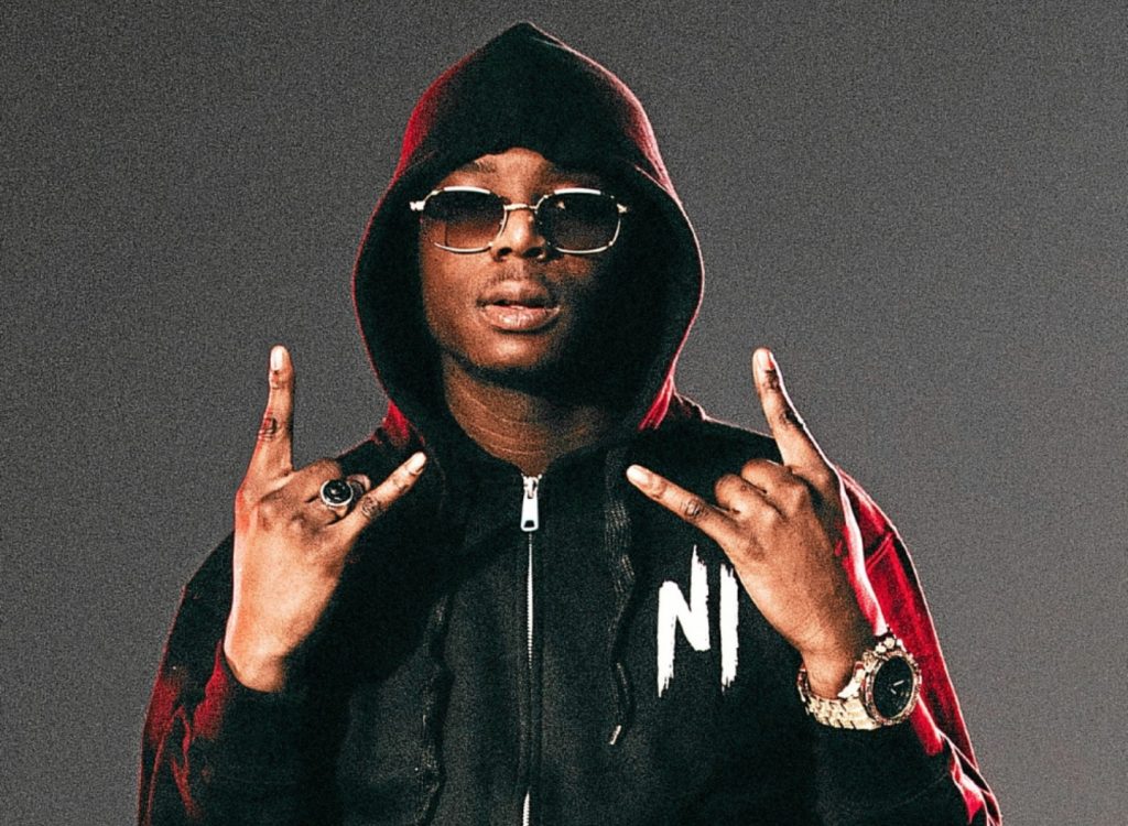 "Artiste hip hop en studio sombre, lunettes jaunes et tenue noire – esthétique brute Vibes Concert"