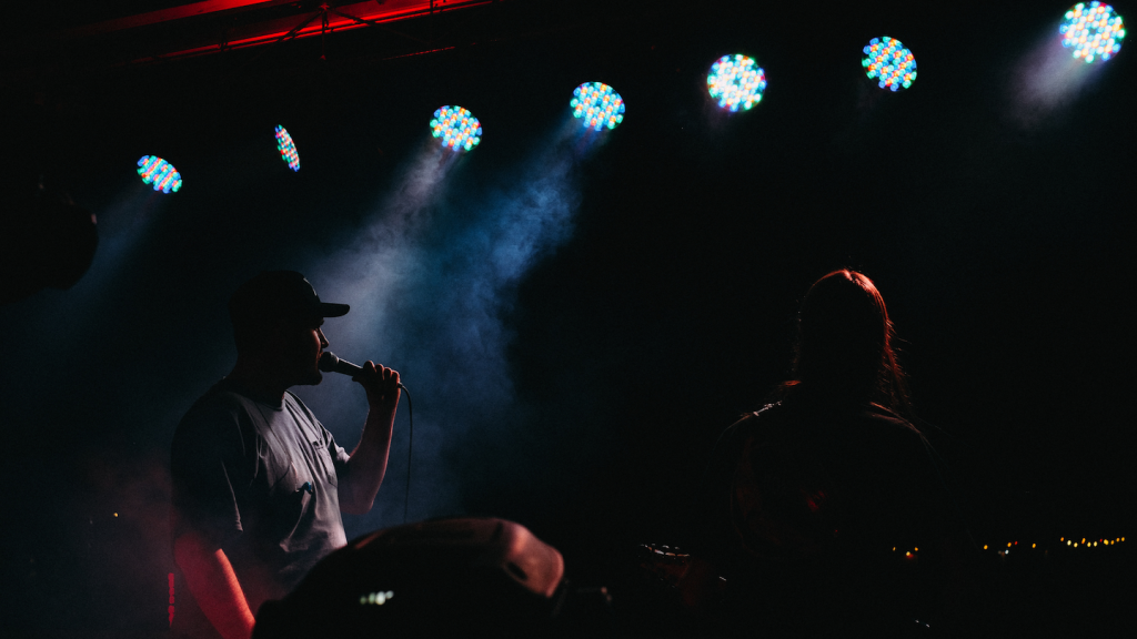 Silhouettes de deux artistes sur scène sous des projecteurs lumineux, illustrant la catégorie musicale Rap.